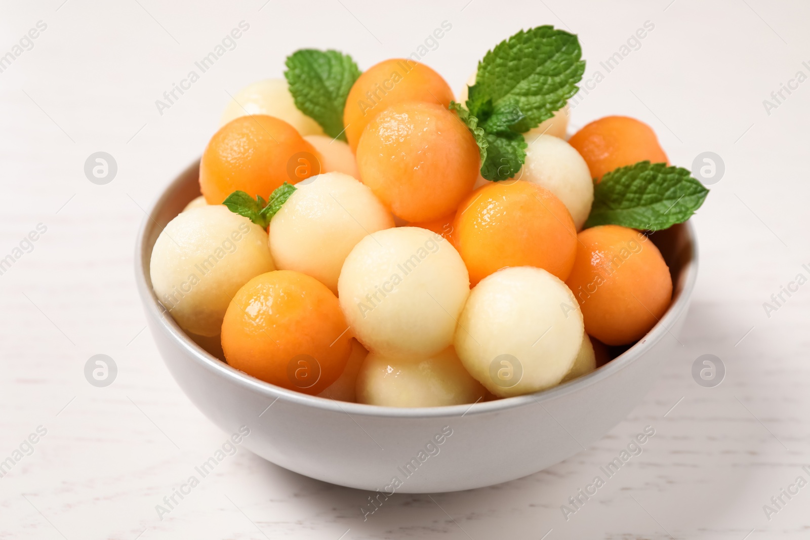 Photo of Melon balls and mint in bowl on white wooden table, closeup