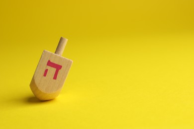 Photo of Wooden dreidel on yellow background, space for text. Traditional Hanukkah game