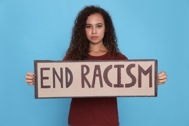 African American woman holding sign with phrase End Racism on light blue background