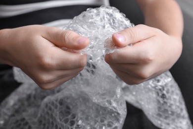 Boy popping bubble wrap indoors, closeup. Stress relief