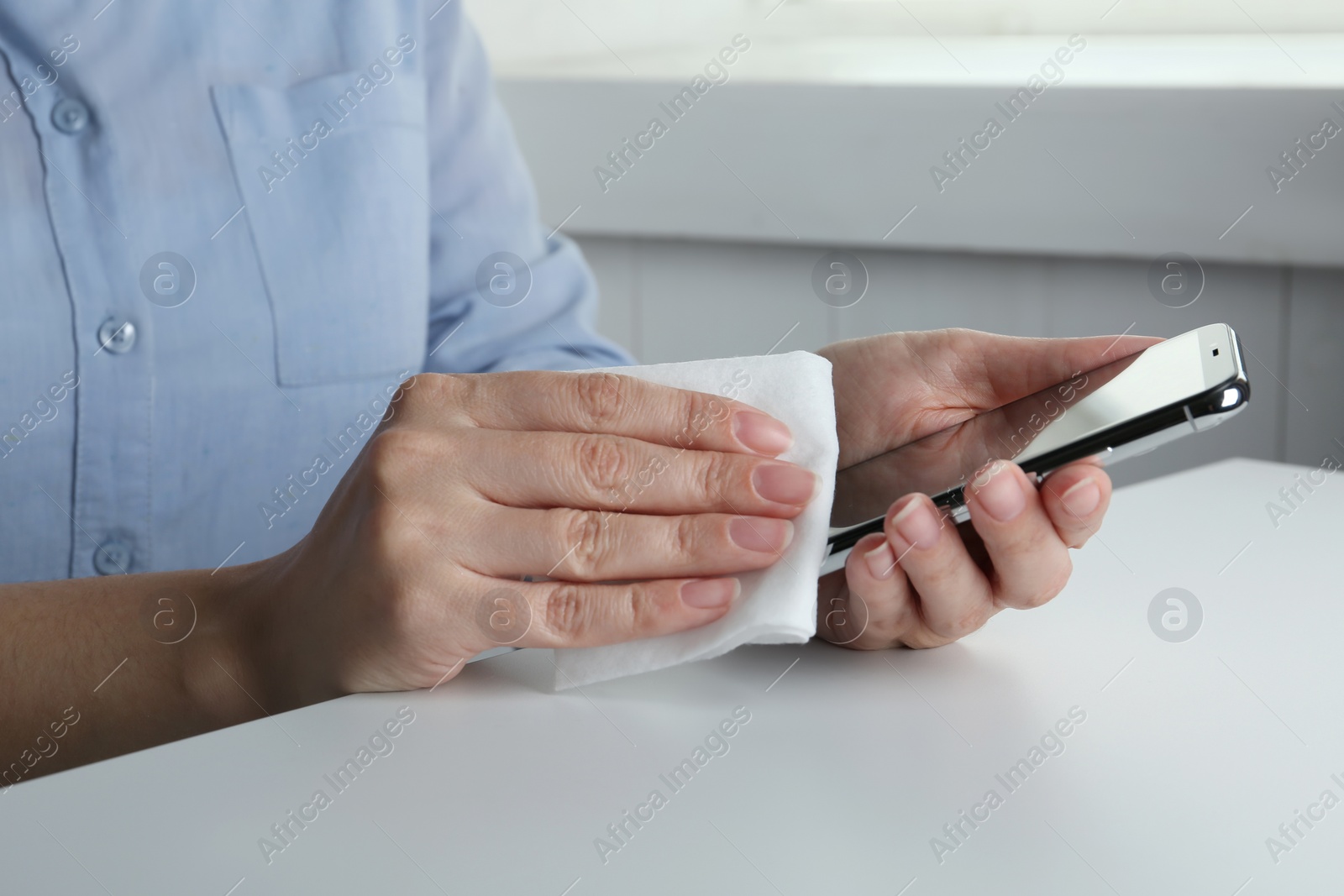 Photo of Woman cleaning smartphone with antiseptic wipe at white table, closeup