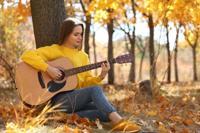 Photo of Teen girl playing guitar in autumn park