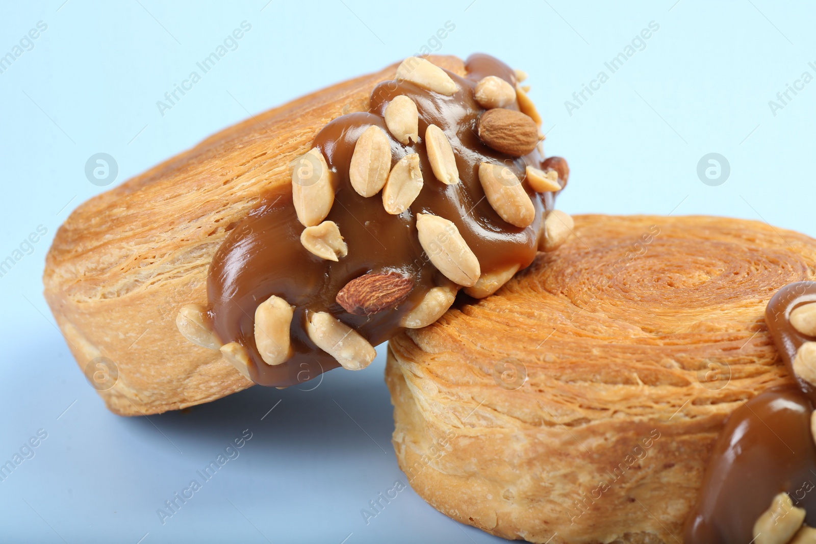 Photo of Supreme croissants with chocolate paste and nuts on light blue background, closeup. Tasty puff pastry