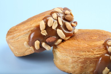Photo of Supreme croissants with chocolate paste and nuts on light blue background, closeup. Tasty puff pastry