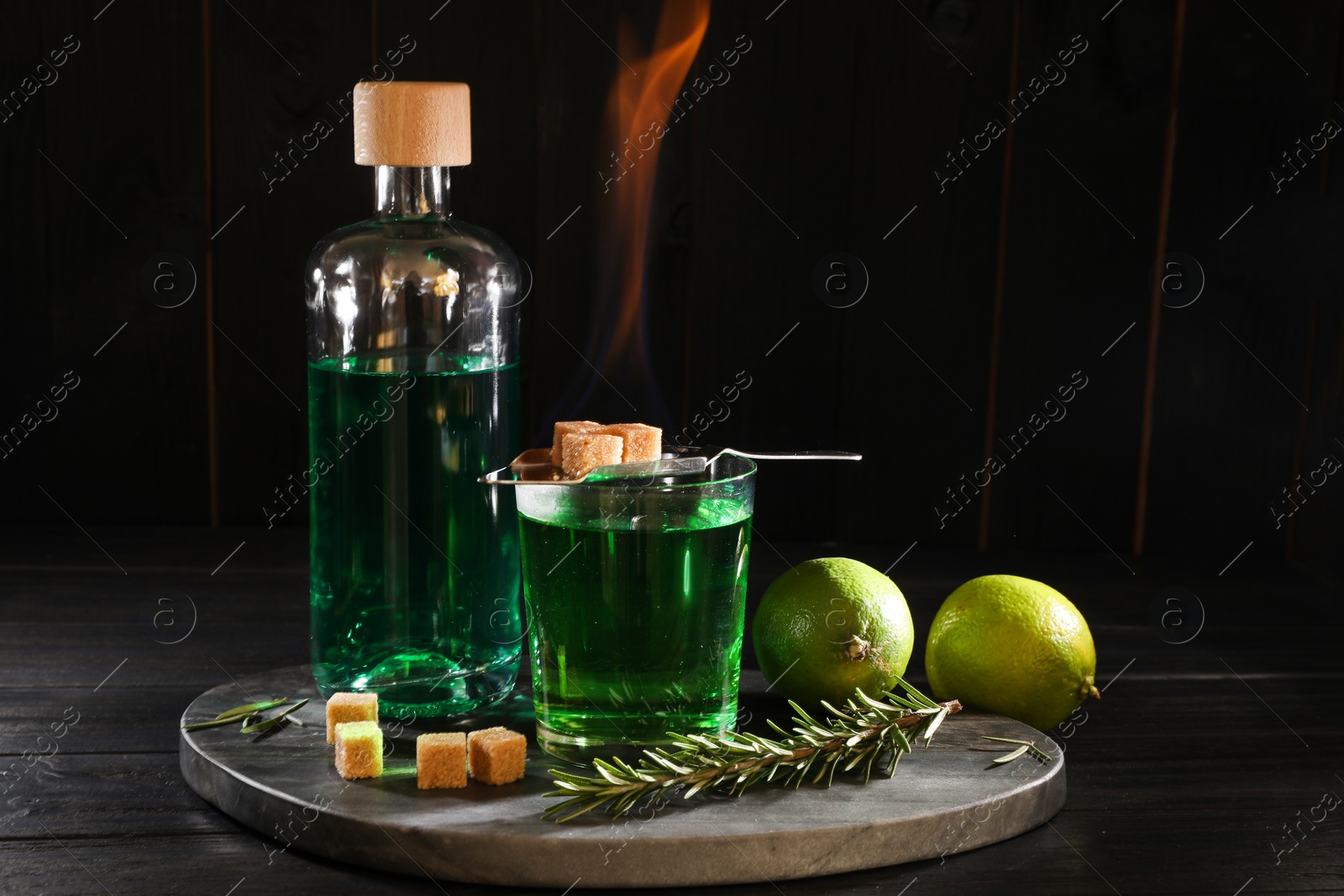 Photo of Absinthe in glass, flaming brown sugar, rosemary and lime on wooden table. Alcoholic drink
