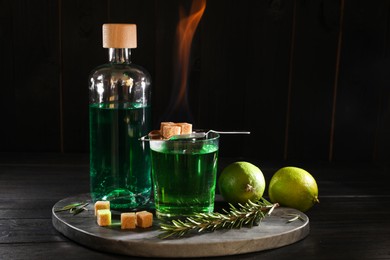 Photo of Absinthe in glass, flaming brown sugar, rosemary and lime on wooden table. Alcoholic drink
