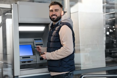 Image of Young man with credit card near cash machine outdoors