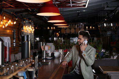 Photo of Young business owner talking on phone in his cafe