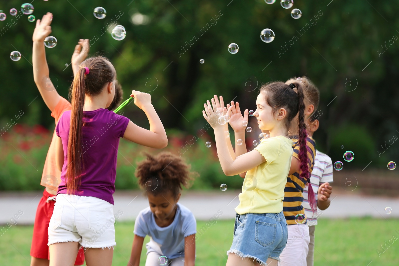 Photo of Cute little children playing with soap bubbles in park