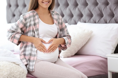 Photo of Happy pregnant woman sitting on bed at home, closeup