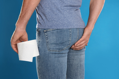 Photo of Man with toilet paper suffering from hemorrhoid on light blue background, closeup