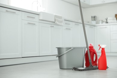 Photo of Mop, detergents and plastic bucket in kitchen, space for text. Cleaning supplies
