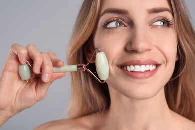 Photo of Young woman using natural jade face roller on light grey background, closeup