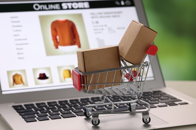 Photo of Mini cart with boxes on laptop, closeup. Online store