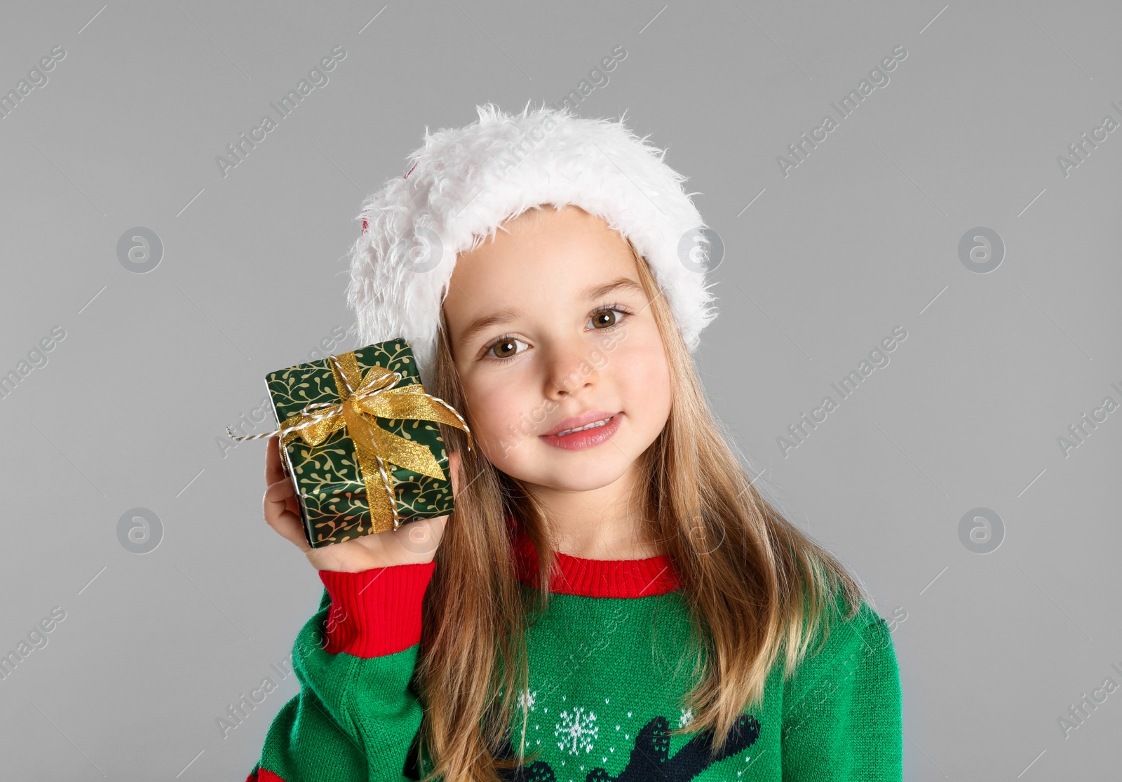 Photo of Cute child in Santa hat with Christmas gift on grey background