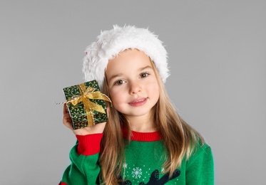 Photo of Cute child in Santa hat with Christmas gift on grey background