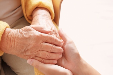 Photo of Helping hands on light background, closeup. Elderly care concept