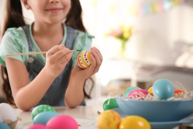 Photo of Little girl painting Easter eggs at table indoors, closeup