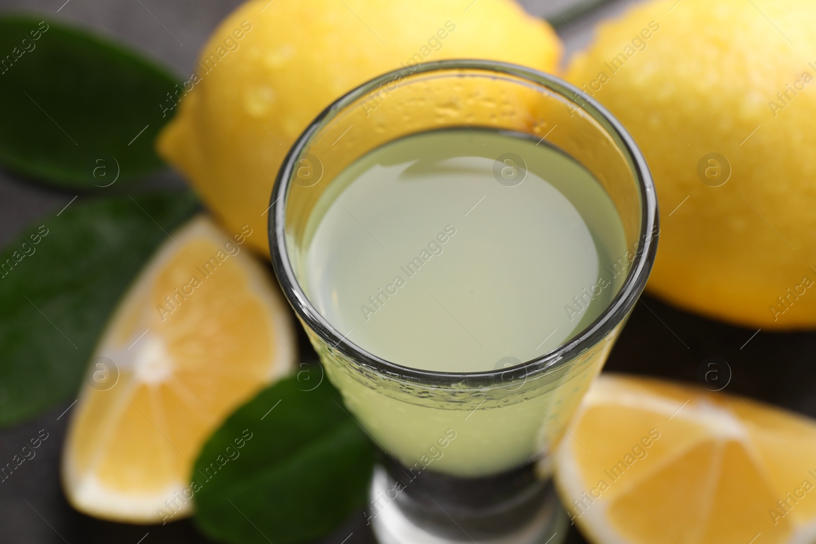 Photo of Tasty limoncello liqueur, lemons and green leaves on table, closeup