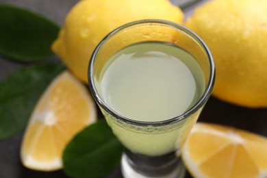 Photo of Tasty limoncello liqueur, lemons and green leaves on table, closeup