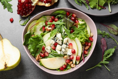 Photo of Tasty salad with pear slices and fresh ingredients on grey table, flat lay