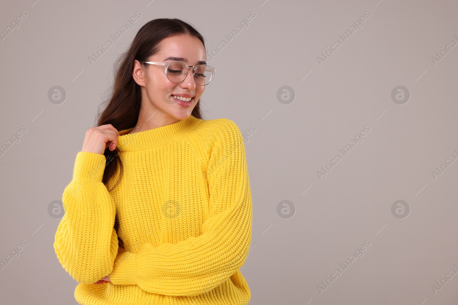 Photo of Beautiful young woman in stylish warm sweater on grey background, space for text