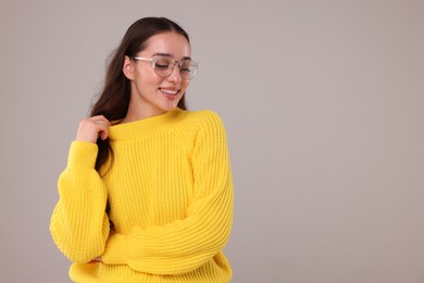 Photo of Beautiful young woman in stylish warm sweater on grey background, space for text