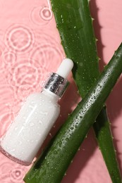 Photo of Bottle of cosmetic product and aloe leaves in water on pink background, flat lay