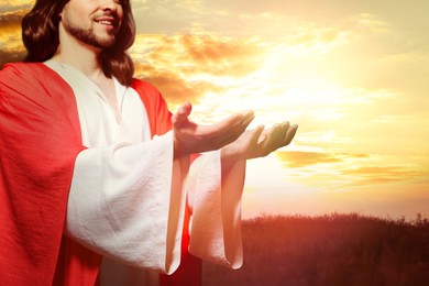 Image of Jesus Christ reaching out his hands and praying at sunset