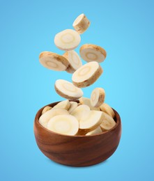Pieces of parsnip root falling into wooden bowl on light blue background