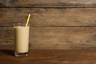 Glass of tasty smoothie with straw on wooden table. Space for text