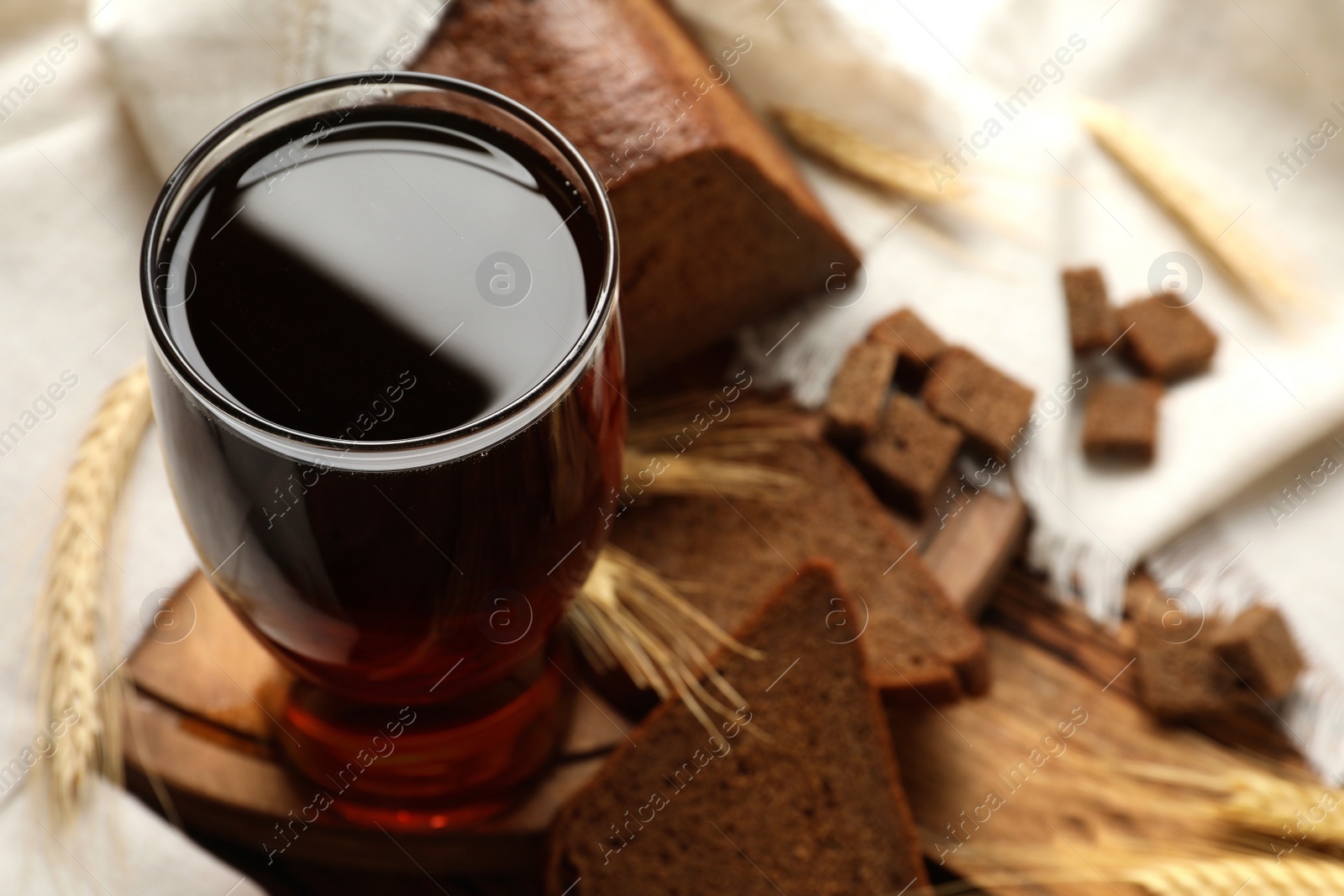 Photo of Glass of delicious kvass, spikes and bread on wooden table. Space for text