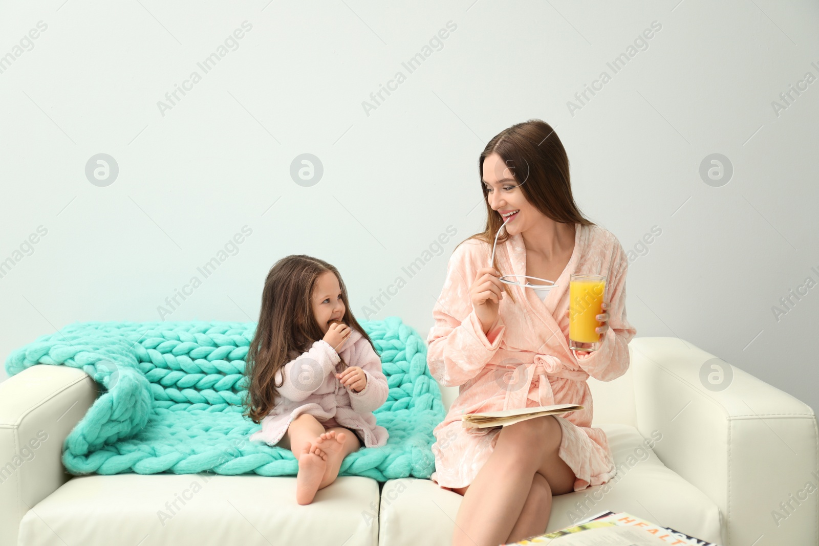 Photo of Mother and daughter in bathrobes sitting on sofa