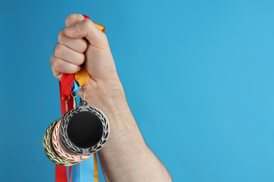 Man holding medals on blue background, closeup. Space for design