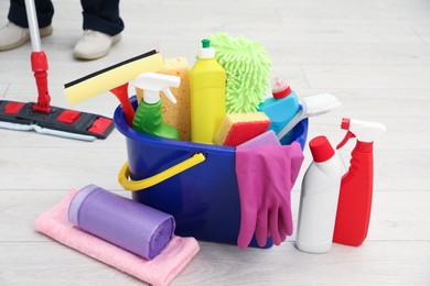 Photo of Different cleaning supplies in bucket and man mopping floor, selective focus