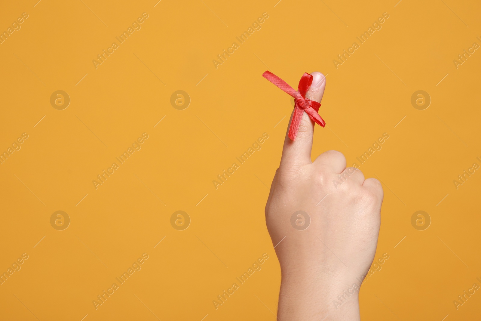 Photo of Man showing index finger with red tied bow as reminder on orange background, closeup. Space for text