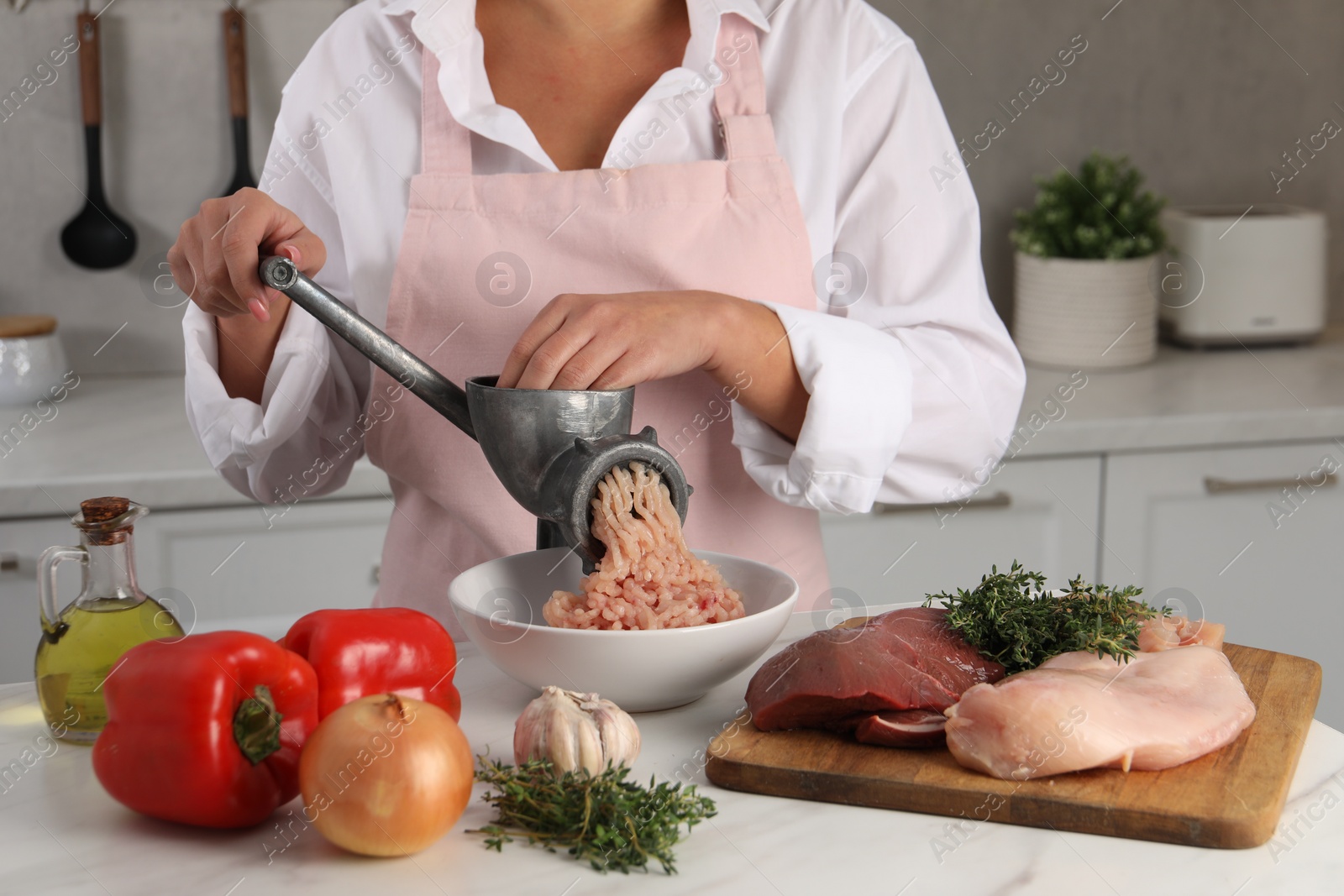 Photo of Woman making chicken mince with metal meat grinder at white table in kitchen, closeup