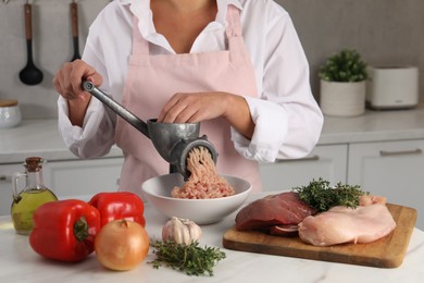 Woman making chicken mince with metal meat grinder at white table in kitchen, closeup