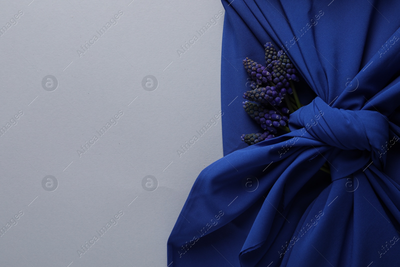 Photo of Furoshiki technique. Gift packed in blue silk fabric and muscari flowers on white table, top view. Space for text