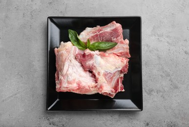 Photo of Plate with raw chopped meaty bones and basil on grey table, top view