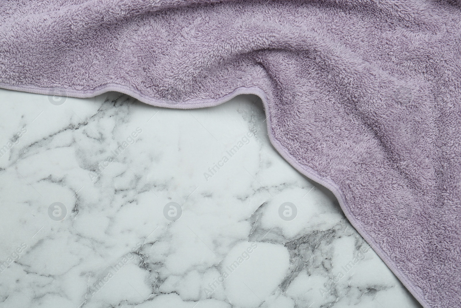 Photo of Violet terry towel on white marble table, top view. Space for text