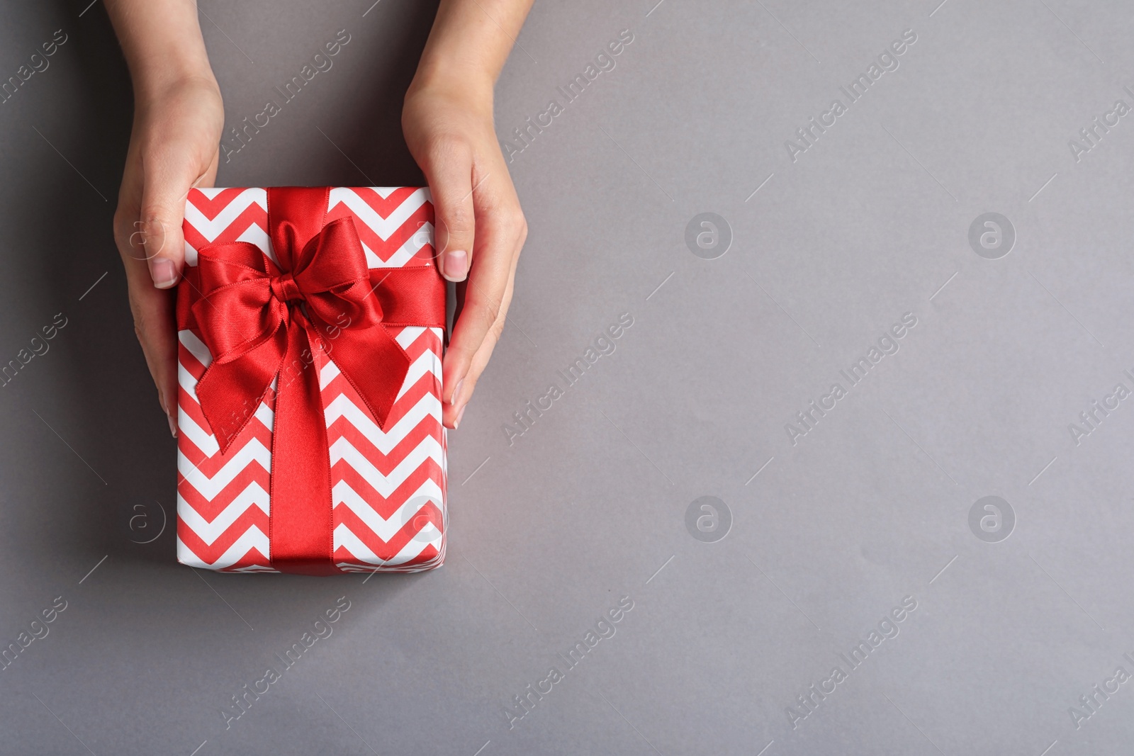 Photo of Woman holding gift box on grey background, top view