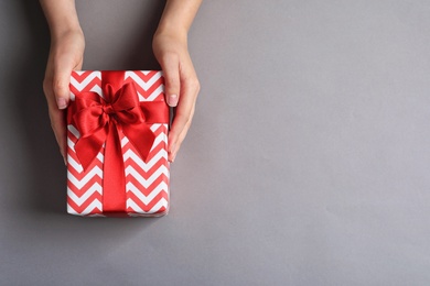 Photo of Woman holding gift box on grey background, top view