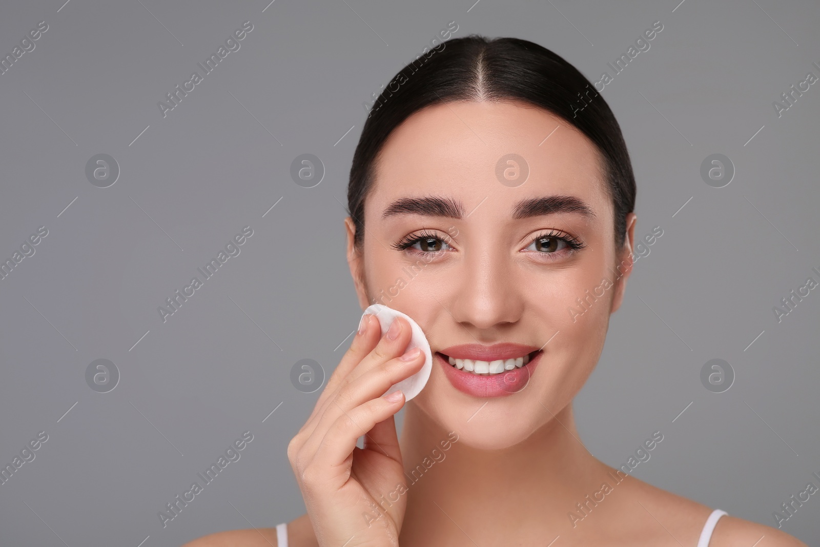 Photo of Beautiful woman removing makeup with cotton pad on gray background, space for text