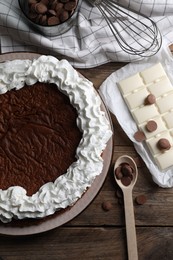 Photo of Delicious homemade sponge cake with cream and different kinds of chocolate on wooden table, flat lay