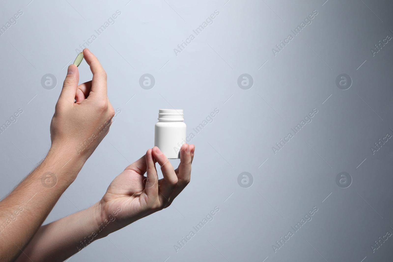 Photo of Man holding pill and bottle on light grey background, closeup. Space for text