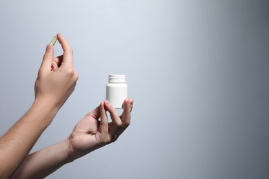 Man holding pill and bottle on light grey background, closeup. Space for text