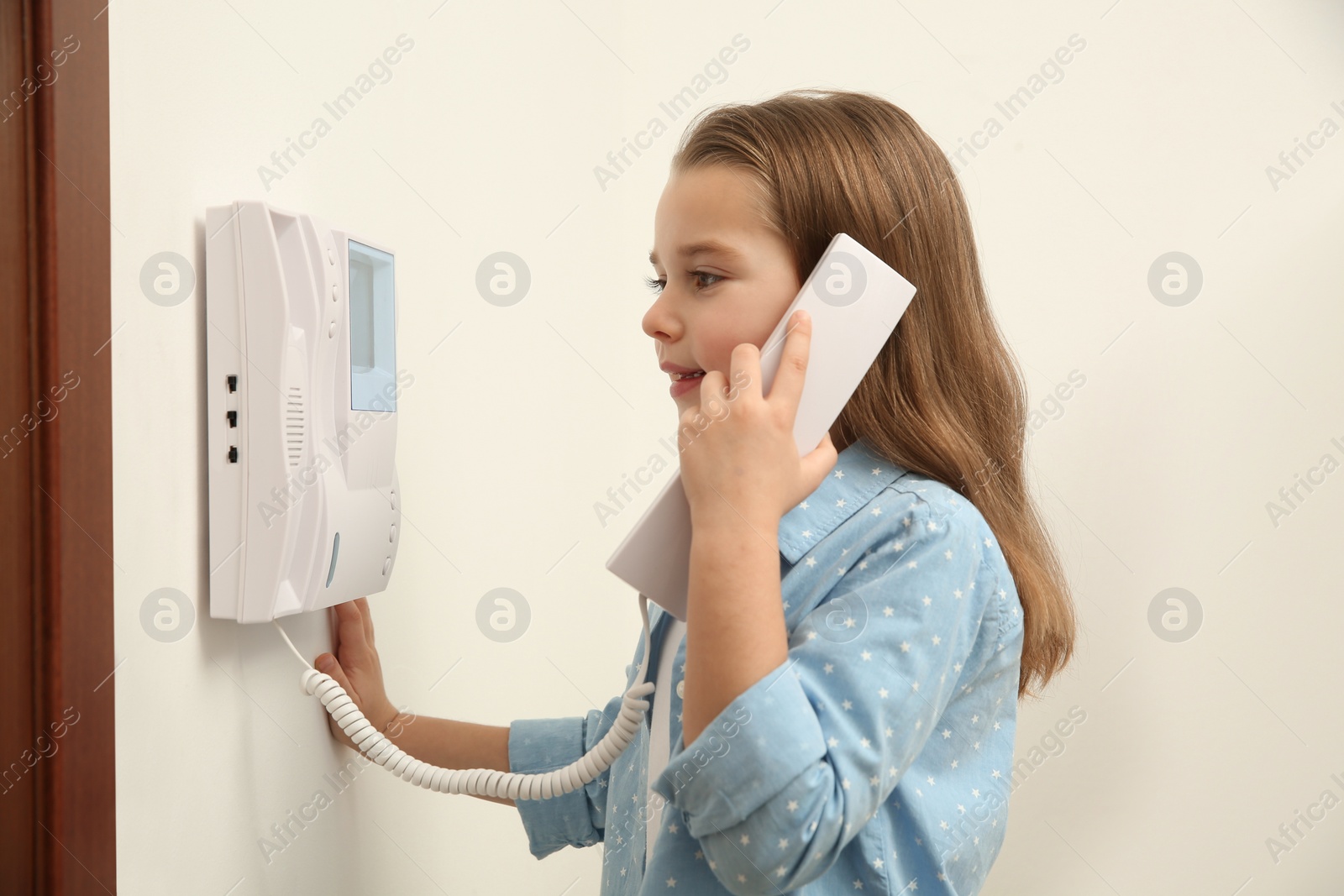 Photo of Cute little girl answering intercom call indoors