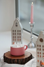 Photo of Beautiful house shaped candle holders and hot dink with marshmallow on windowsill indoors, space for text