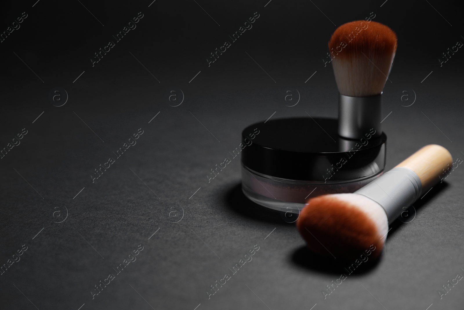Photo of Face powder and makeup brushes on black background, closeup. Space for text
